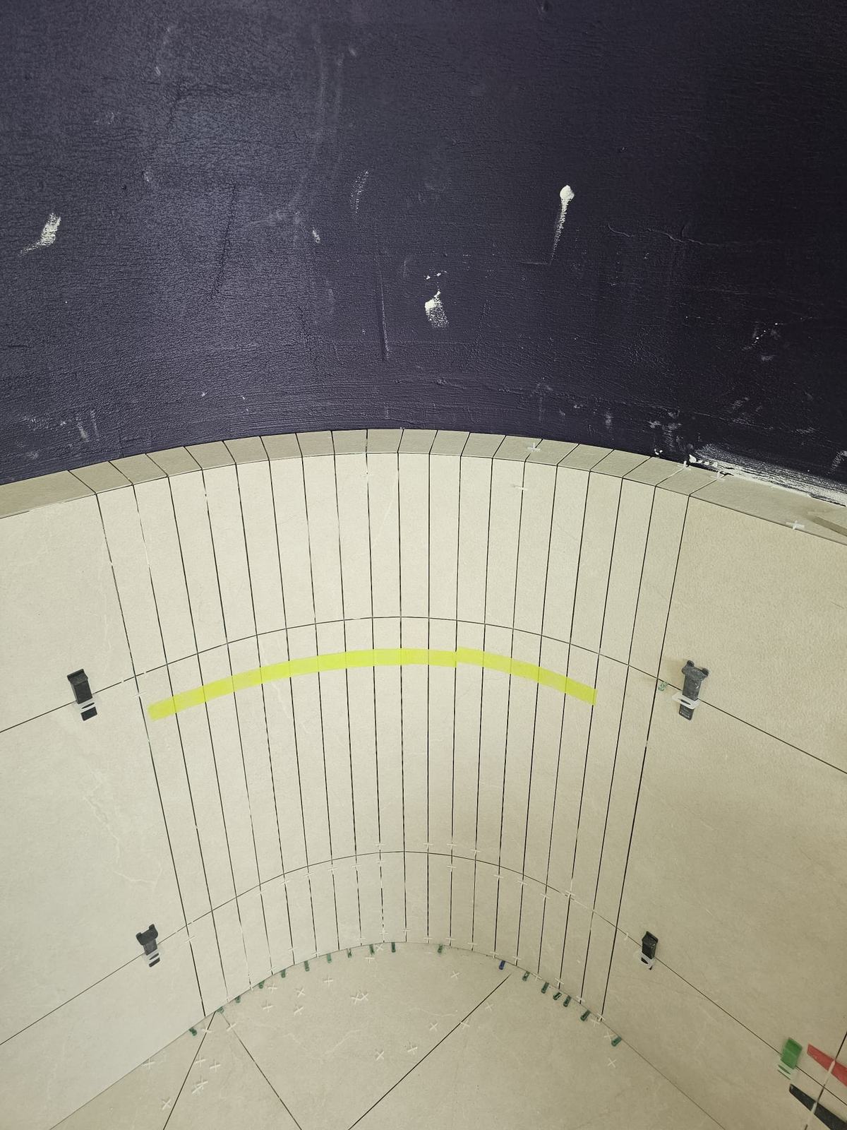 Curved shower wall part-way through tiling, with levelling clips in place